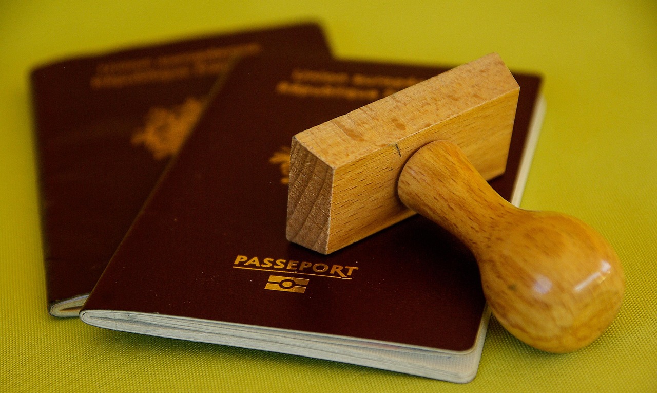 A wooden passport stamp rests on top of two closed dark red passports on a green surface.