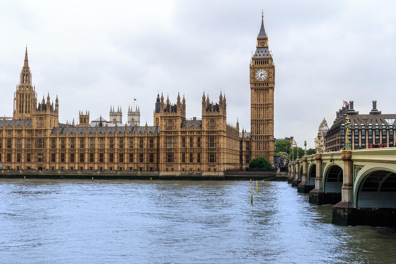 The Palace of Westminster and Big Ben standing beside the River Thames under a cloudy sky in London.