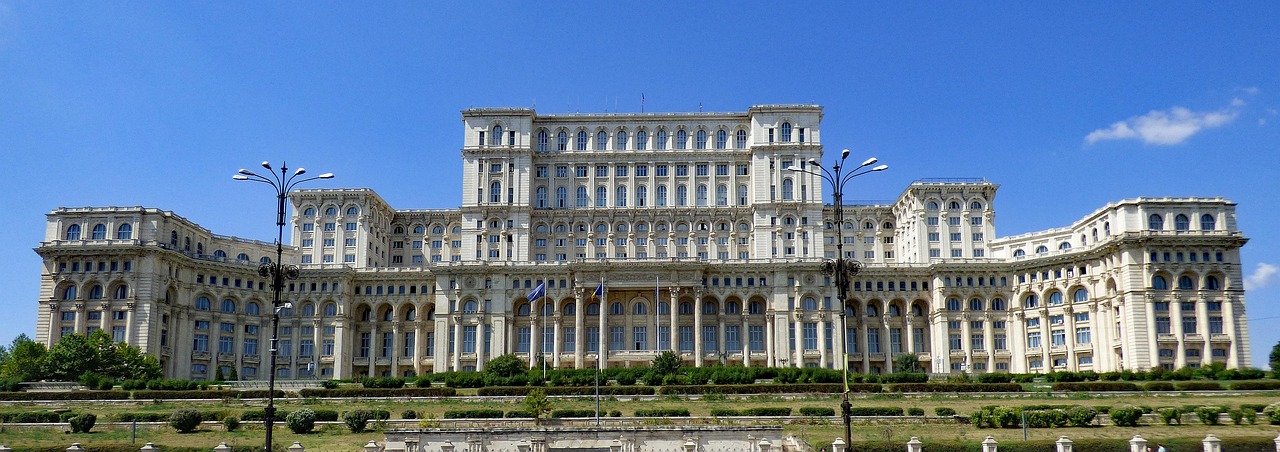 The Palace of the Parliament in Bucharest, a massive white neoclassical building under a clear blue sky.