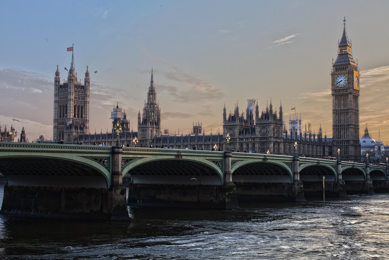 A wide view of the Palace of Westminster and Big Ben clock tower next to the Westminster Bridge over the River Thames at dusk.